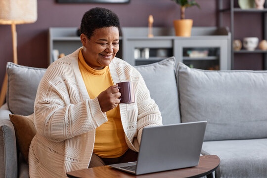 Portrait of senior black woman using laptop at home and enjoying cup of coffee, copy space
