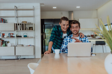 Obraz premium A young married couple is talking to parents, family and friends on a video call via a laptop while sitting in the living room of their modern house
