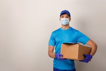 Fototapeta na wymiar Portrait of handsome attractive delivery man in a medical mask and gloves holding card-board box. Express delivery service. Copy space.