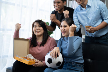 Group of Asian man and woman friends watching soccer games world cup competition on television with...