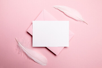 Holiday greeting card mockup with pink envelope and white feather on light pink background, top...