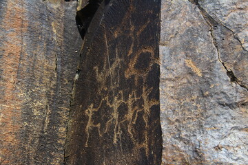 Images of dancing ancient people are carved on a flat vertical stone, petroglyphs, ancient rock paintings in the Tamgaly-Tas tract in summer
