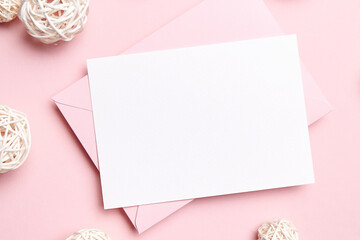 Holiday greeting card mockup with pink envelope and decoration on light pink background, top view, flat lay. Blank wedding invitation or Valentine Day letter, empty card