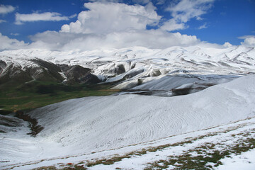 Panorama on the snow-covered plateau of Assy with snow-covered mountain ranges, green areas of the mountains, with the sky and beautiful clouds