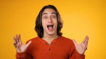 Portrait of amazed gender fluid young man 20s shocked, saying WOW. Handsome guy with long hair surprised isolated on solid yellow background.