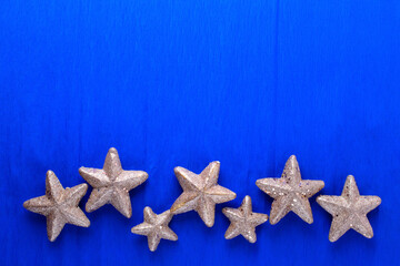 Fototapeta na wymiar Border from big and small golden decorative stars on blue paper textured background. Top view. Christmas, New Year holidays concept. Place for text.
