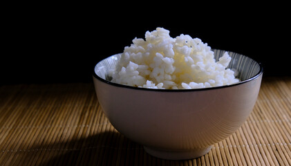 Bol de arroz cocinado en fondo negro de bambú. Dark food