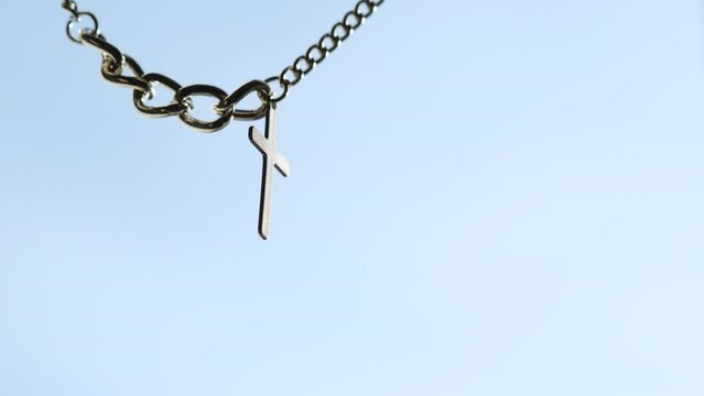 Silver or stainless steel necklace with cross pendant hanging on sky background.
