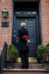 Person holding a gift of red roses, outside at the front door