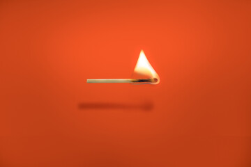 A single matchstick is burning on an orange background.