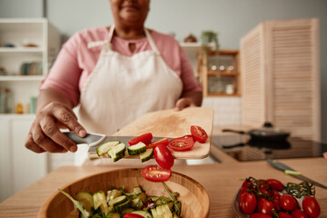 Close up of black senior woman putting vegetables in bowl while making salad in kitchen, copy space