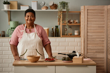 Front view portrait of black senior woman in kitchen interior smiling at camera happily, copy space