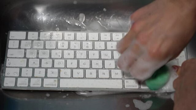 Cleaning and washing the dirty computer  keyboard under tap water -    crazy house cleaning to sanitize from viruses - paranoia and increased fears after Covid-19 Coronavirus epidemic
