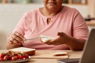 Close up of black woman making sandwich while enjoying breakfast in cozy kitchen, copy space