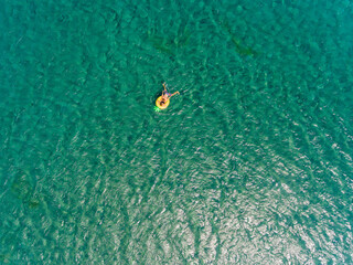 Fototapeta na wymiar Aerial view of a couple swimming at turquoise water of Aegean Sea with a yellow swimming ring