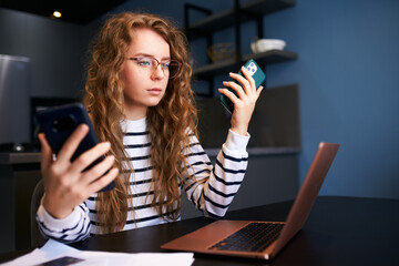 Curly blonde woman in glasses working from home with multiple electronic internet devices....