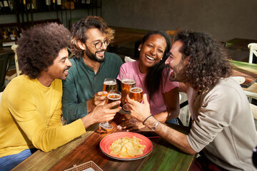 A group of colleague workers toast with beer in the restaurant bar after work at the pub happy hour. Happy friends having fun together drinking alcohol indoors.