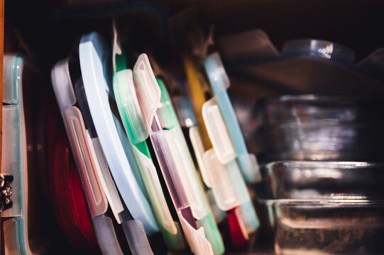 Narrow Depth Of Field Picture Of An Open Kitchen Cabinet With An Assortment Of Containers And Mismatched Lids Stacked.