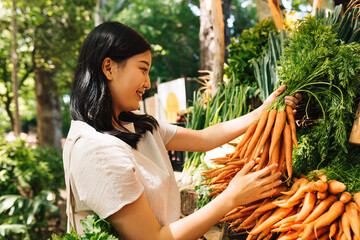Smiling buyer holding a bunch of carrots. Asian woman choosing vegetables in the local market.