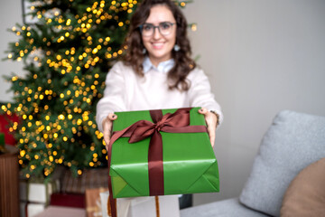 A green box with a gift in the hands of a cute girl with glasses
