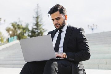 A man in a suit sits on the steps of a city staircase with a laptop. Working break. outdoors. business lifestyle