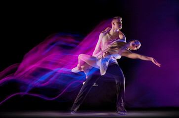 Portrait of young man and woman, figure skating athletes dancing isolated over black background in neon with mixed lights