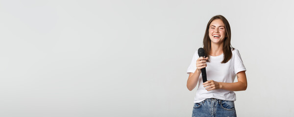Happy laughing girl holding microphone and singing karaoke, white background