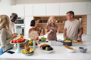 Group of senior diverse friends gathered around kitchen island while preparing meal