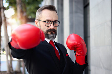 Senior mature businessman wearing red boxing gloves or mitt punch, metaphors about fight business...