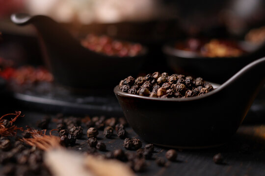 Spices and herbs on dark background, dried black pepper seeds in tablespoon with assorted colorful of seasoning ingredients as blurred background