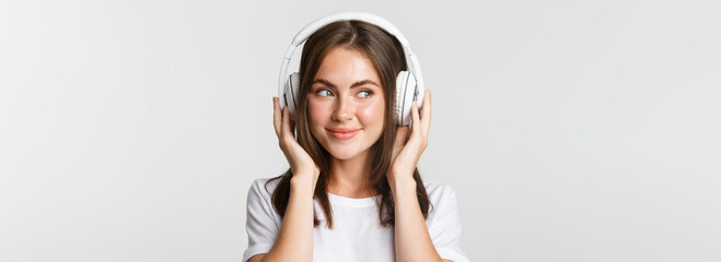 Close-up of smiling attractive brunette girl listening music in headphones, enjoying interesting...