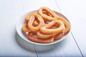 Churros caseros dulces junto aún tazón de chocolate sobre una mesa blanca rústica