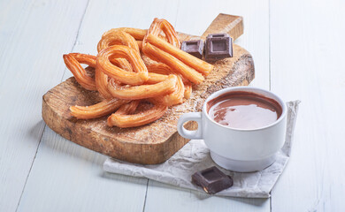 Churros caseros dulces junto aún tazón de chocolate sobre una mesa blanca rústica