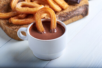 Churros caseros dulces junto aún tazón de chocolate sobre una mesa blanca rústica