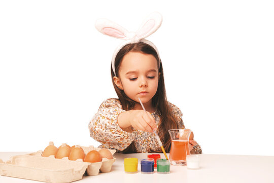 Concentrated cute little girl is painting some eggs for the coming Easter in a white studio.