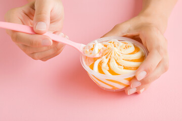Young adult woman hand holding spoon and eating swirl white vanilla and yellow fruit ice cream on...