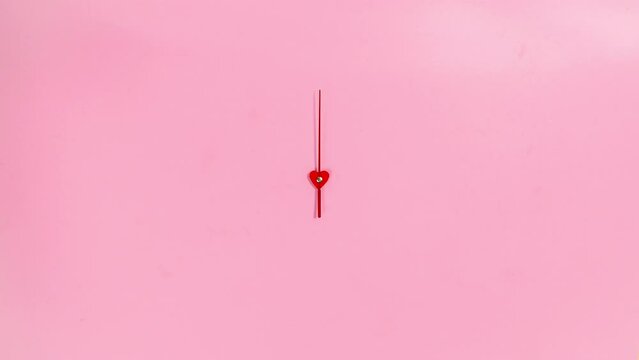 4k The red hand of the clock rotates in a circle. Pink background. The concept of the transience of time. Heart in the center. Stop motion animation. Copy space. Flat lay.