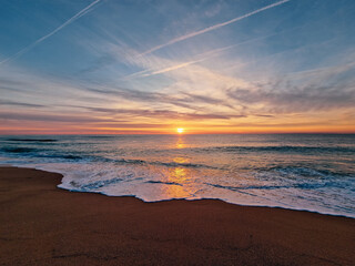 Salida del sol desde la playa con estelas en el cielo