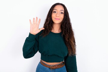 Obraz premium teen girl with curly hair wearing green sweater over white background showing and pointing up with fingers number five while smiling confident and happy.