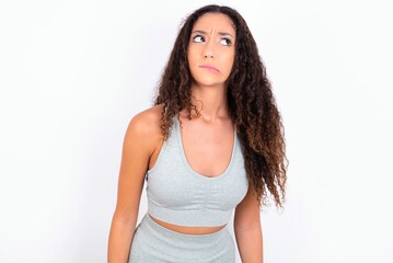 Beautiful teen girl with curly hair wearing grey sport set over white background making grimace and crazy face, screaming out of control, funny lunatic expressing freedom and wild.