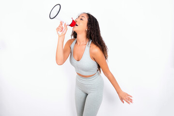 Beautiful teen girl with curly hair wearing green sport set over white background Through Megaphone with Available Copy Space