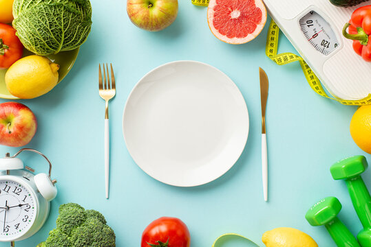 Proper nutrition concept. Top view photo of plate fork knife scales vegetables fruits alarm clock dumbbells and tape measure on isolated pastel blue background with empty space
