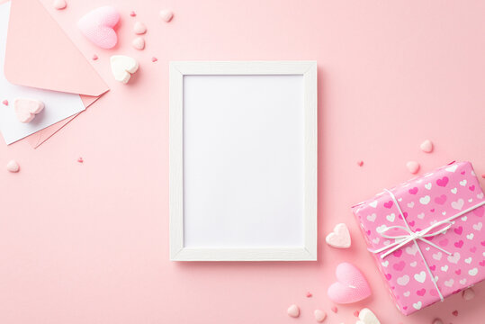 Valentine's Day concept. Top view photo of white photo frame envelope with letter giftbox heart shaped marshmallow candle and sprinkles on isolated pastel pink background with empty space