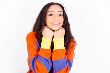 Satisfied beautiful teen girl wearing striped knitted sweater over white background touches chin...