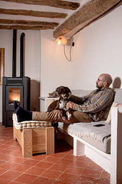 luxury rustic design dining room, on the sofa a man and his dog, pellet cooker lit with flame, white and wood colours