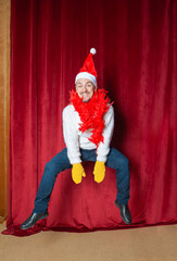 Fototapeta premium Funny handsome smiling man wearing Santa hat jumping on the red curtain background