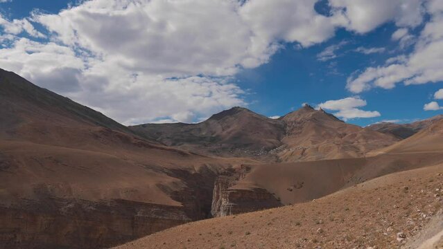 4K shot of Gorge canyon at Dry mountains of Spiti Valley with view of Chicham village. Dry rugged Himalaya mountains of Spiti, Himachal Pradesh, India. Mountains in background of blue cloudy sky.
