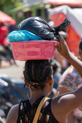 Scenes from the Haitian market near the border with Haiti. Haitian Woman carrying a plastic bucket willed with goods on her head shot from behind.
