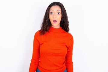 Obraz premium Emotional attractive teen girl wearing knitted red sweater over white background with opened mouth expresses great surprise and fright, stares at camera. Unexpected shocking news and human reaction.