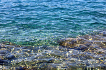 Transparent sea surface with stones on a bottom. Rocky beach, turquoise water for background